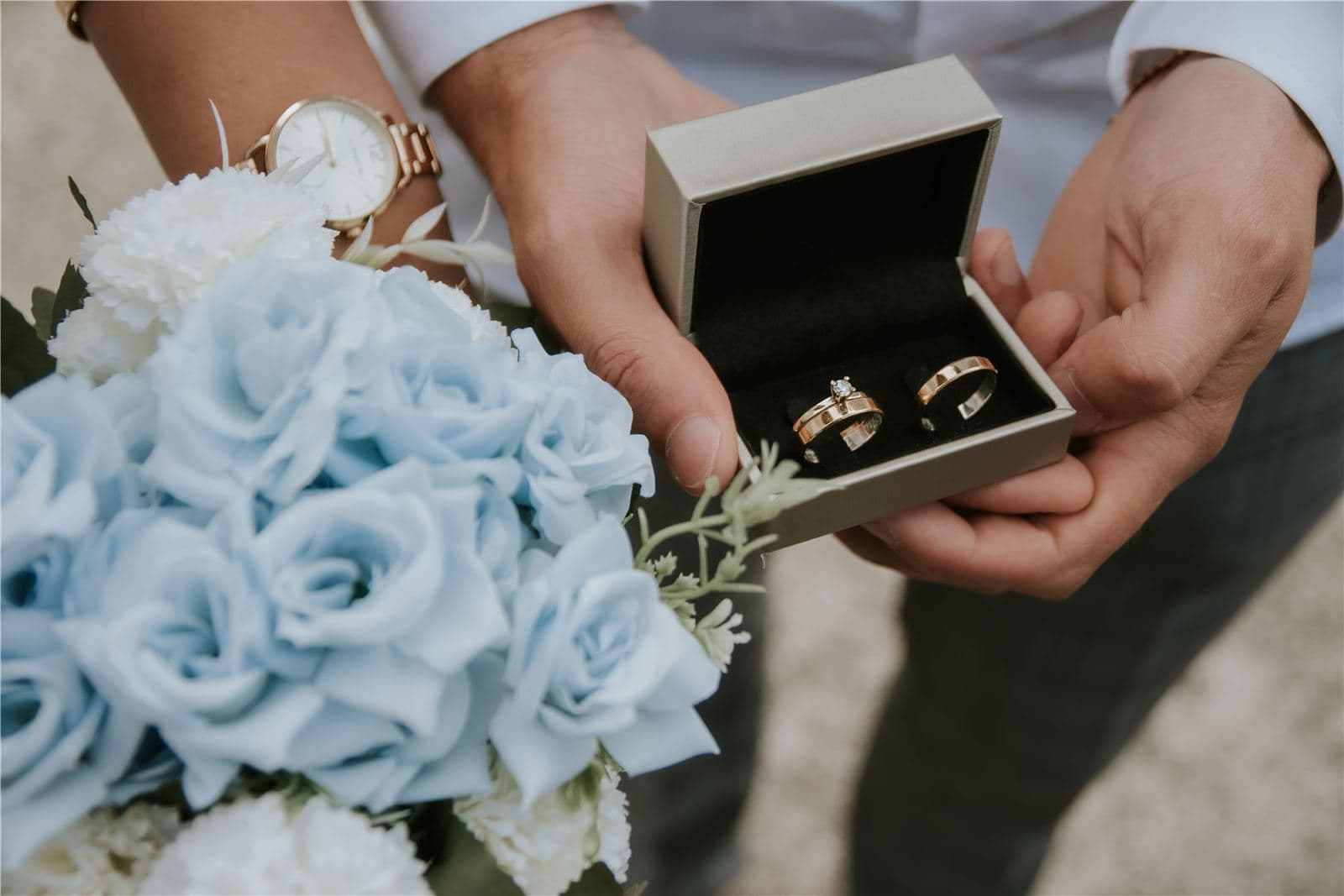 Wedding rings in a box held next to a blue and white bouquet